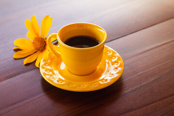 Uma xícara amarela com café e um girassol sobre uma mesa de madeira.