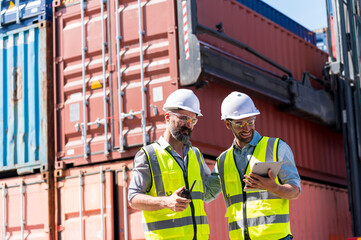Logistics engineer and inspector working togetter and discussing with Shipping container stacker background in commercial transport port