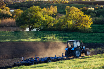 a farm tractor cultivates the land against the background of a beautiful rural landscape