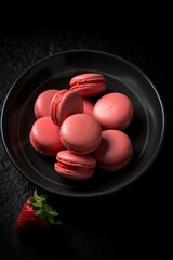 strawberry macaron, on a black plate and black background, top view