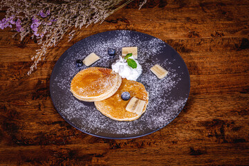 A stack of banana pancakes with slices of fresh bananas, walnuts and honey on top with cup of tea on a wooden background. A healthy breakfast. Copy space