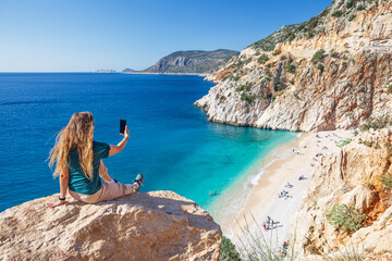 Young woman making selfie photo by smartphone over Kaputas beach, Lycia coast. Summer day walk by Lycian way at family vacation in Mediterranean Sea, Kas, Antalya region, Turkey