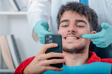 young patient at the dentist looking at her teeth with mobile phone