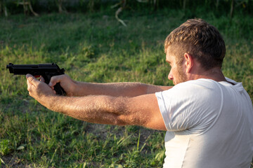 a caucasian man stands and aims a gun on the street on a summer day