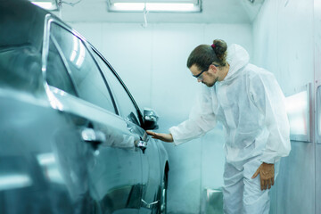 Professional automotive painting technician in chemical protecting suit inspecting car painting quality in painting chamber together. Car painting and detailing technicians portrait.