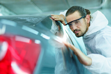 Professional automotive painting technician in chemical protecting suit inspecting car painting...