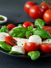 Caprese salad with ripe tomatoes and mozzarella cheese with fresh basil leaves on black background. Italian food. Close-up