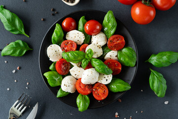 Top view of Caprese salad with ripe tomatoes and mozzarella cheese with fresh basil leaves on black background. Italian food