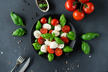 Caprese salad with ripe tomatoes and mozzarella cheese with fresh basil leaves on black background. Italian food. Top view