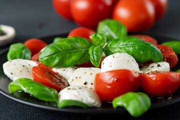 Caprese salad with ripe tomatoes and mozzarella cheese with fresh basil leaves on black background. Italian food. Close-up