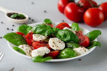 Caprese salad with ripe tomatoes and mozzarella cheese with fresh basil leaves on light background. Italian food. Close-up