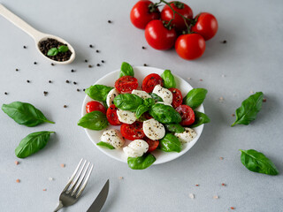 Italian Caprese salad with sliced tomatoes, mozzarella cheese, basil, olive oil on light background. Vegetarian food