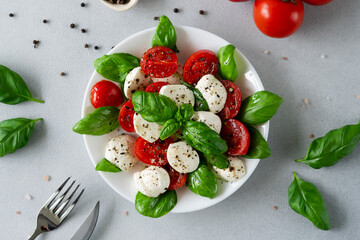 Top view of Caprese salad with ripe tomatoes and mozzarella cheese with fresh basil leaves on light background. Italian food. Copy space for text