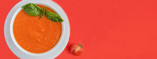 Tomato soup in the white bowl on the red background. Top view. Copy space.