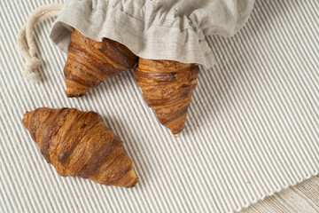 Croissant in linen eco bag. Cotton bag with croissants on wooden background.