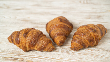 Three fresh croissants on white rustic table. Homemade golden croissants on brown wooden table.Three fresh croissants on white rustic table. Homemade golden croissants on brown wooden table.