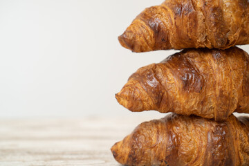 Stack of freshly baked croissants on wooden table. Home-made buttery croissants stacked on top of each other on brown table.