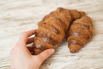 Hands tearing a fresh croissant. Croissants turn apart. Croissant in wooman hand on wooden table.
