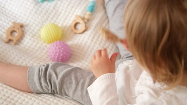 Cute baby girl playing tactile wooden toys. Young child hand plays sensory massage ball. Enhance the cognitive, physical process. Brain development. Support for Children with ADHD, autism, fidgeting.