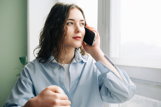 Caring wife by the window eagerly awaiting her husband's arrival. Anxious wife calling her husband while keeping an eye on the clock. Loving wife anxiously awaiting her husband's return from work.