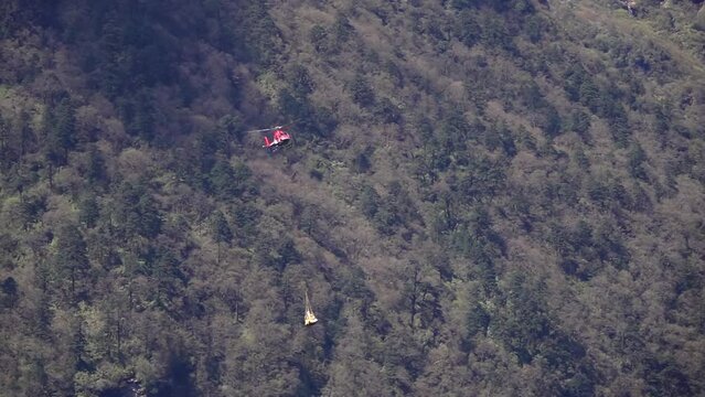 Red helicopter carrying load in midair, Nepal
Slow motion shot from Nepal over forest, 2023
