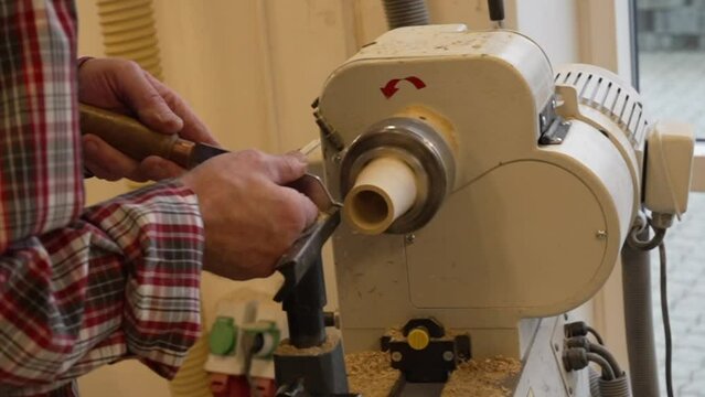 Man carpenter using chisel for shaping piece of wood on turning lathe machine with many shavings at workshop - close up. Carpentry, hobby, craftsmanship and woodworking concept