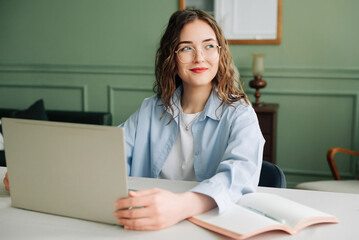 Smiling female corporate employee working on laptop in modern office, marketing manager or...
