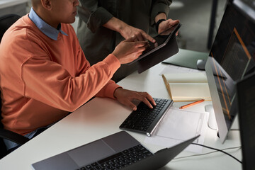 High angle view of colleagues discussing online presentation on digital tablet while working with computer codes at table