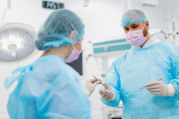 a nurse in a sterile glove hands scalp surgical instruments to a surgeon during an operation in a hospital