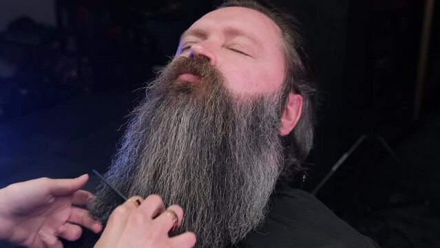 The barber girl's hand combs a man's beard with a comb