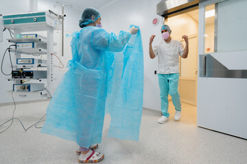 The nurse helps the surgeon put on a sterile gown before surgery uniform in the operating room...