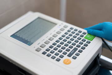 a cardiologist enters data on the display of an ECG machine to perform a cardiogram procedure of a patient's heart in a clinic