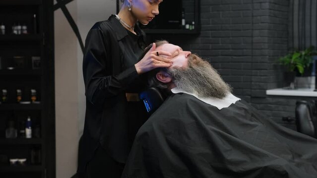 a stylist girl in a barbershop puts a moisturizer on the client's face.