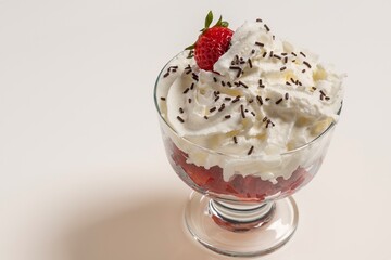 Delicious dessert glass of strawberries with cream and chocolate chips on white background.