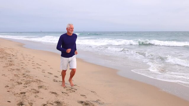 A mature 66 year old man jogging at the beach in Southern California. Slow Motion.