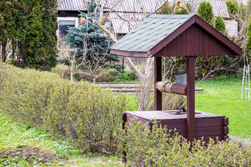 Naklejka premium A wooden water well with a green roof sits in a garden.