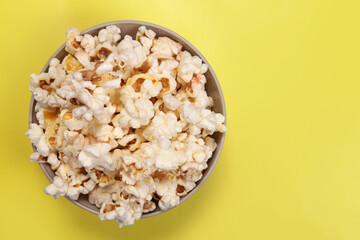 Paper cup with popcorn on yellow background, top view
