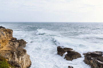 Fototapeta na wymiar Coastline with atlantic ocean in Cascais, Portugal. Waves at the shore and rocky hills