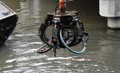 Old bicycles being removed from a canal by a mechanical grab in Amsterdam, Netherlands. 