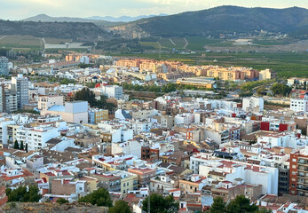 Fototapeta na wymiar Buildings, houses and streets in city, aerial view. View of rooftops and streets of city of Sagunto in Spain. Town against backdrop of mountains. Roofs of houses and roofs from side of Sagunto Castle.