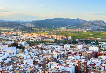 Buildings, houses and streets in city, aerial view. View of rooftops and streets of city of Sagunto in Spain. Town against backdrop of mountains. Roofs of houses and roofs from side of Sagunto Castle.
