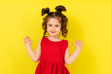 Cute little happy girl in a red dress stands on a yellow background. card, banner. lifestyle. space...
