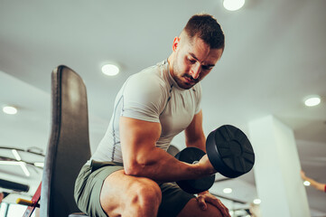 Low angle view of a strong weightlifter pumping biceps while lifting a dumbbell.