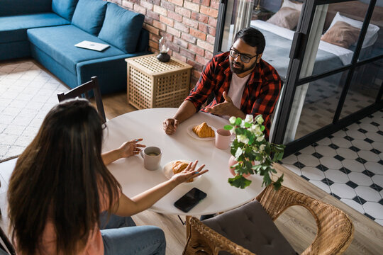 Young diverse loving couple eating croissant and talks together at home in breakfast time. Communication and relationship concept