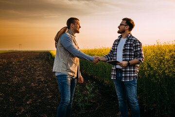 Two business man shake hands on a field.