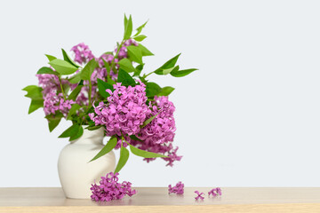 In a white gypsum vase is a bouquet of lilacs. On a wooden table.