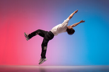 guy acrobat doing back fat in new lighting, male dancer jumps and falls in the air on red blue background