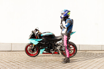 Obraz na płótnie Canvas guy motorcyclist in professional protective equipment and helmet stands near sports motorcycle against white wall