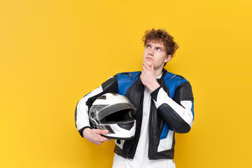 pensive guy motorcyclist in leather jacket holds helmet and thinks on yellow isolated background
