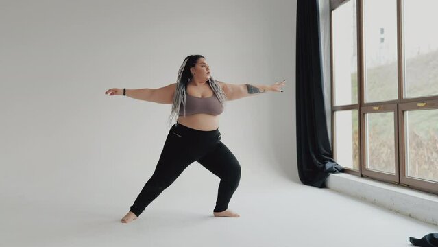 Beautiful overweight female doing exercise Happy body positive fat woman with dreadlocks doing yoga in the gym. Concept of natural diverse beauty and sport. Stout over weight female stretching